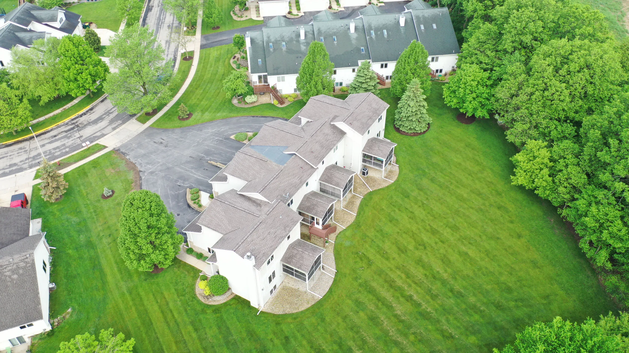 Aerial view of a residential neighborhood showing two rows of townhouses surrounded by green lawns and trees.